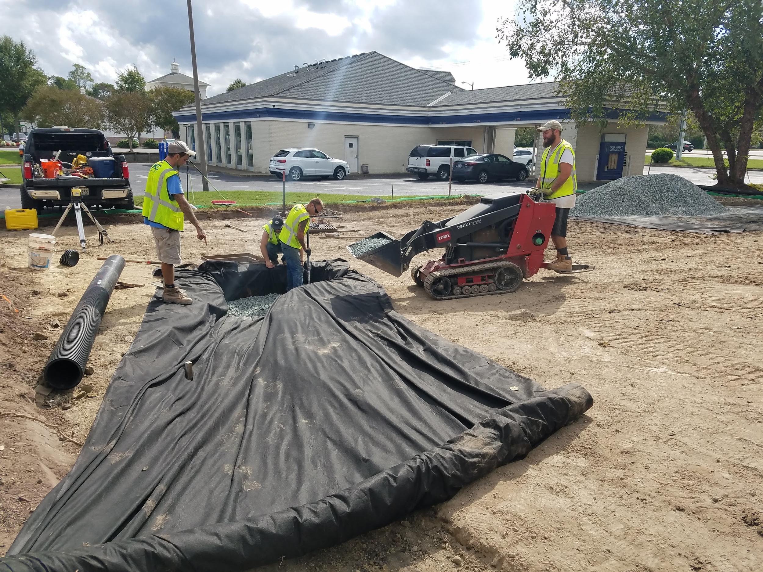 The crew places stone within the fabric-lined drainage excavation.